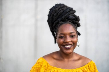 Gri duvarın önünde rastalı saçları olan güzel genç bir kadın.