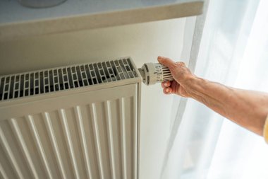 Elderly woman adjusting the heating on a radiator in her home, close-up
