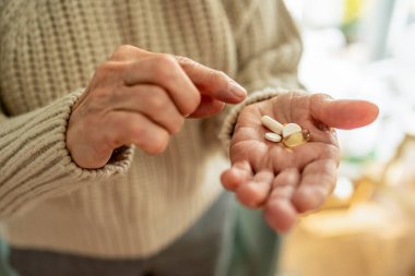 Senior woman taking her medication at home, close-up of hands