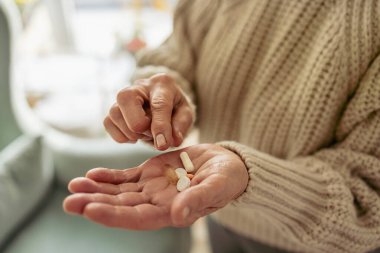 Senior woman taking her medication at home, close-up of hands
