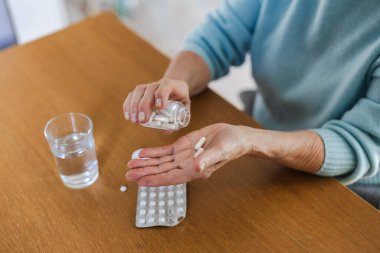 Senior woman taking her medication at home, close-up of hands
