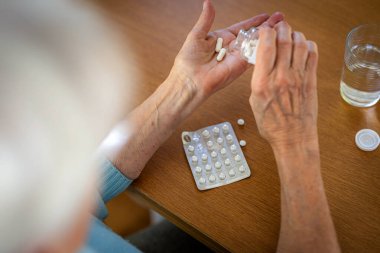Senior woman taking her medication at home, close-up of hands