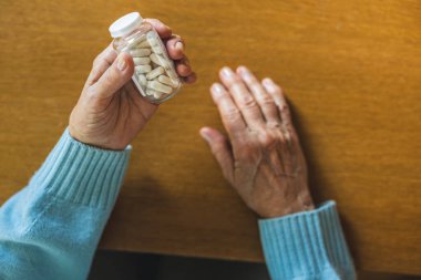 Senior woman taking her medication at home, close-up of hands
