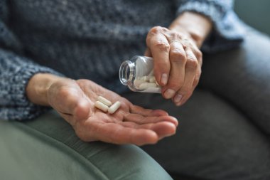 Senior woman taking her medication at home, close-up of hands
