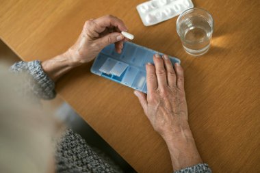 Senior woman taking her medication at home, close-up of hands