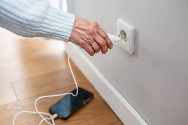 Close-up of senior woman inserting a power plug into a socket to charge her phone