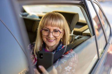 Üst düzey kadın arka koltukta akıllı telefon kullanıyor.