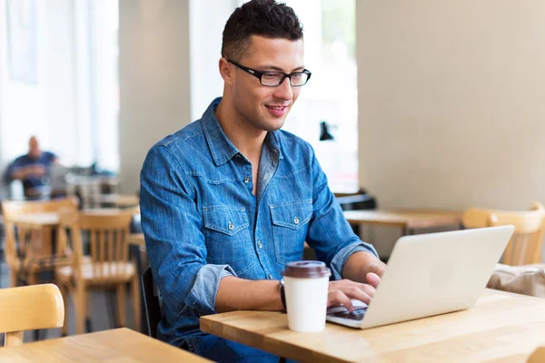 Joven usando el ordenador portátil en la cafetería —  Fotos de Stock