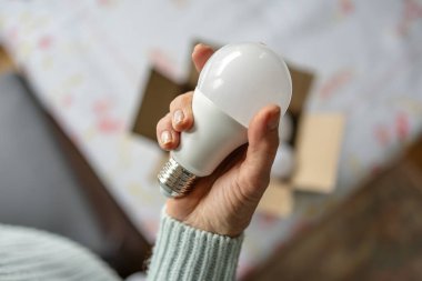 Çevre dostu bir ampulü tutan yaşlı bir kadının elleri