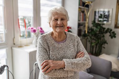 Oturma odasında duran yaşlı kadın gülümsüyor.