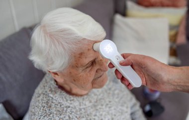 Hemşire evde yaşlı bir kadının ateşini ölçüyor.