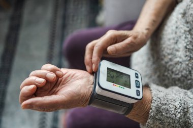 Evde dijital tansiyon monitörü kullanarak kan basıncını ölçen yaşlı bir kadın.