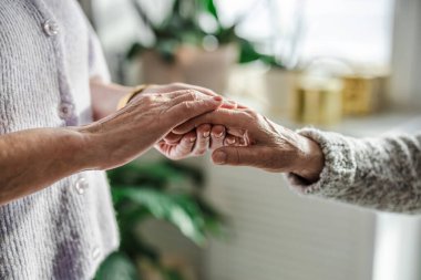 Huzurevinde bakıcısıyla el ele tutuşan yaşlı bir kadın.