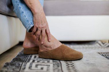 Evdeki kanepede otururken ayak bileği ağrısından muzdarip yaşlı bir kadın.