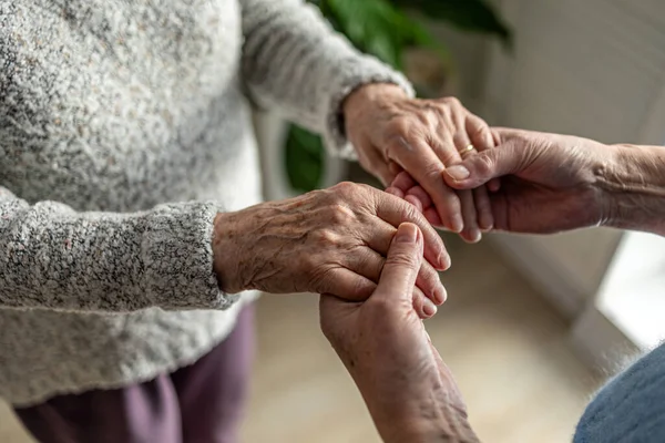 Huzurevinde bakıcısıyla el ele tutuşan yaşlı bir kadın.