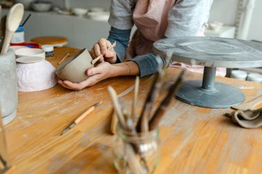 Atölyesindeki kil nesnelerle çalışan bir çömlekçinin ellerine yakın plan.
