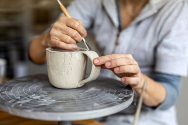 Atölyesindeki kil nesnelerle çalışan bir çömlekçinin ellerine yakın plan.