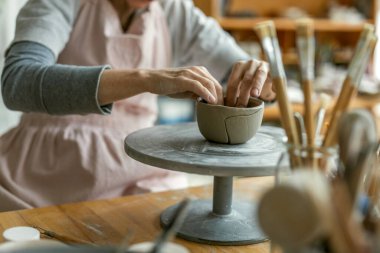 Atölyesindeki kil nesnelerle çalışan bir çömlekçinin ellerine yakın plan.