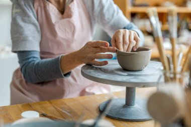 Atölyesindeki kil nesnelerle çalışan bir çömlekçinin ellerine yakın plan.