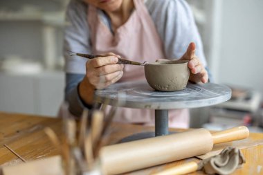 Atölyesindeki kil nesnelerle çalışan bir çömlekçinin ellerine yakın plan.