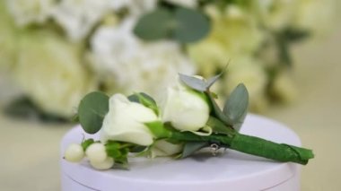 Damadın düğün yaka çiçeği ve yüzükleri beyaz bir stantta dönüyor..