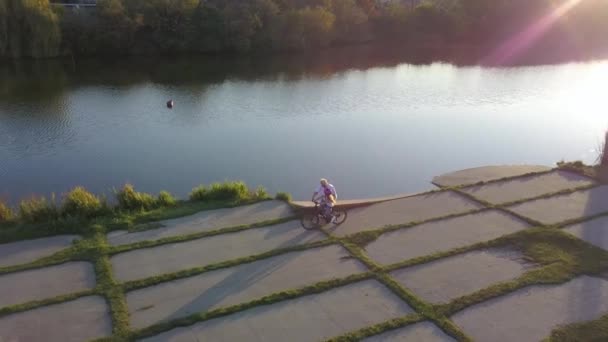祖母は孫娘に湖の近くで自転車に乗る方法を教えています 最上階だ コッパーの上で撃つ — ストック動画