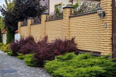 Dekoratif modern sarı tuğlalı çit. Konut binasının yanında tuğla sütunlar var.