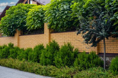 Dekoratif modern sarı tuğlalı çit. Konut binasının yanında tuğla sütunlar var.