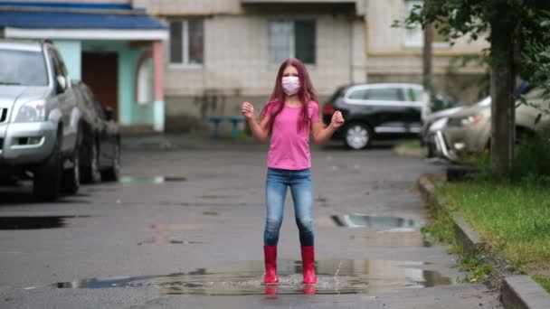 의료용 마스크와고 무부츠를 소녀가 자동차들 사이에 주거용 건물의 마당의 웅덩이 — 비디오