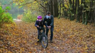 Genç bir baba kızına koruyucu kaskla bisiklet sürmeyi öğretiyor. Yüzlerinde tıbbi maskeler var. Covid-19 koronavirüs salgını sırasında yürüyüş.