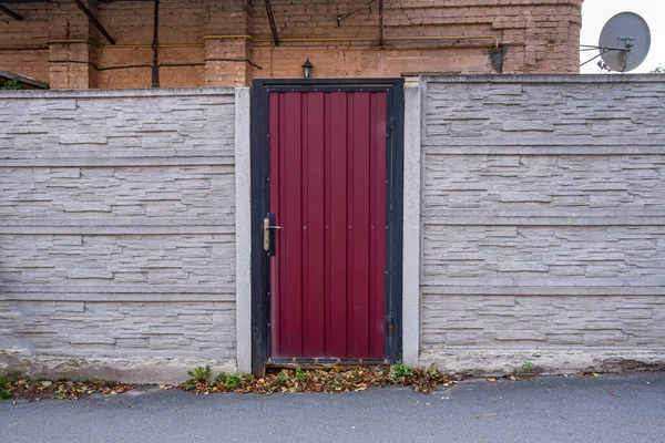 Um pequeno portão de ferro ondulado vermelho colocado em uma cerca de concreto. — Fotografia de Stock