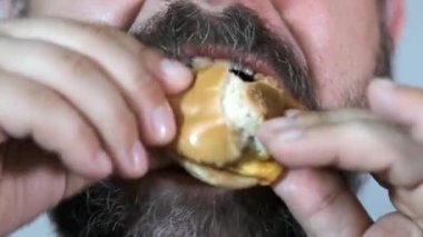 Yetişkin sakallı adam besleyici bir hamburger yiyor. Abur cubur. Yakın plan. Seçici odak.