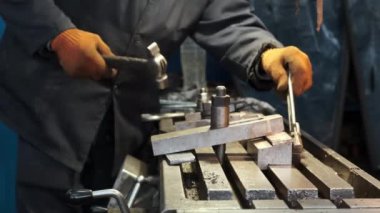 Turuncu eldivenli bir işçi, fabrikadaki eski bir atölyede çekiç ve ingiliz anahtarıyla vidaları söküyor. Eller yakın plan..
