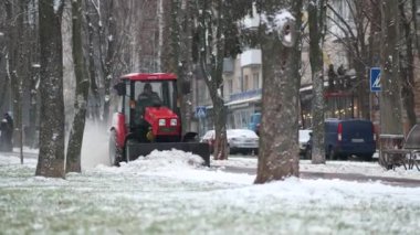 Küçük bir traktör kış günü kentteki kaldırımlardan karı temizler. Modern kar temizleme ekipmanları.