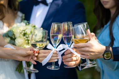 Gelin, damat ve misafirler doğada şampanya bardaklarını yakın çekimde tutarlar..