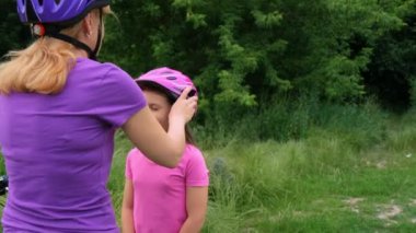 Annem yazın parkta kızının koruyucu bisiklet kaskını takıyor. Bisiklet sürmeyi öğreniyorum. Mutlu çocukluk.