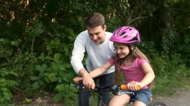 Ağabeyi küçük kız kardeşine parkta bisiklet sürmeyi öğretiyor. Mutlu spor ailesi..