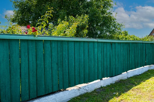 The old weathered wooden green fence near residential homes.