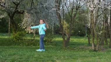 Küçük bir kız, düşen yaprakların arasında çiçek açan bir ağacın yanında dönüyor. yavaş çekim.