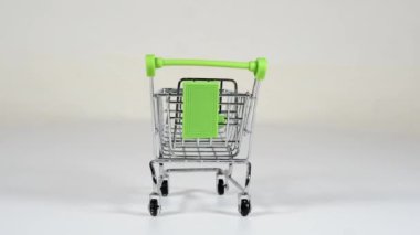 Yeşil saplı metal dekoratif küçük alışveriş arabası beyaz arka planda dönüyor. Yukarıdan bir sürü hap düşüyor. Levhalarla doludur..