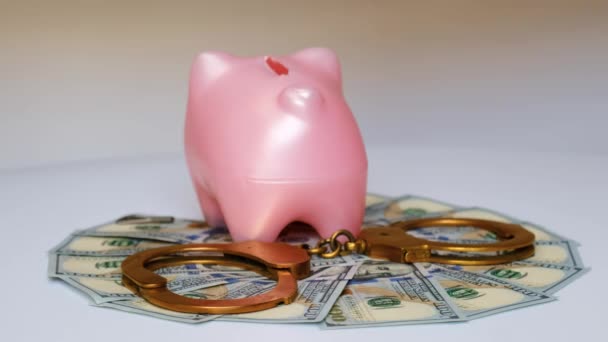 金の手錠 ピンクの貯金箱 そして100ドル札は白い背景で回転します 腐敗と経済犯罪の概念 — ストック動画