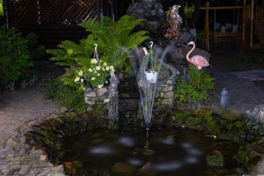 Geceleri bahçesinde flamingo ve baykuş heykelleri olan doğal taştan yapılmış dekoratif çeşme..