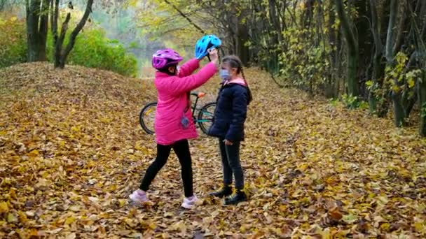 Dívka pomáhá své sestře nasadit si bezpečnostní přilbu před jízdou na kole za slunečného podzimního dne v přírodě a dává si plácačky. Bezpečnost, sport, rekreace — Stock video
