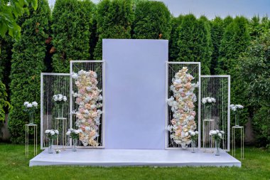 Bahçede çiçeklerle süslenmiş beyaz bir düğün kemeri.