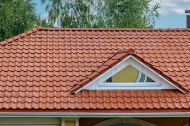 Binanın çatısının beyaz çerçeveli bir penceresi ve üçgen çatısı olan kırmızı fayanslı bir bölümünün yakın çekim görüntüsü.