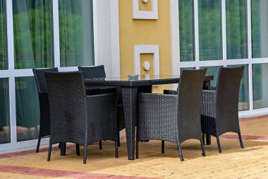 Cam sehpası olan siyah bir hasır veranda ve binanın dışındaki tuğla bir verandaya yerleştirilmiş sandalyeler.