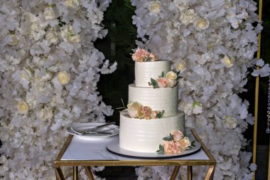 Üç katlı beyaz pasta, pembe güller ve yeşil bir masa.