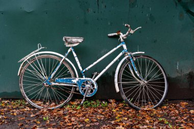 Beyaz koltuğu ve yeşil bir duvara yaslanmış gidonu olan mavi beyaz bir bisiklet.