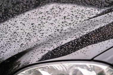 Bir arabanın farının ve kaputunun yakın plan fotoğrafı. Yüzeyinde su damlacıkları var. Yakın zamanda yağmur yağdığını gösteriyor.