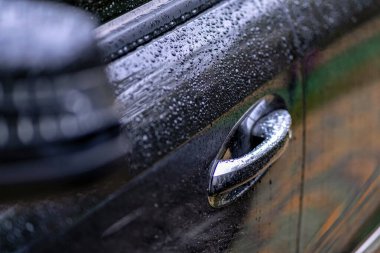 Yüzeydeki su damlacıklarını gösteren bir arabanın kapı kolunun yakın plan fotoğrafı.